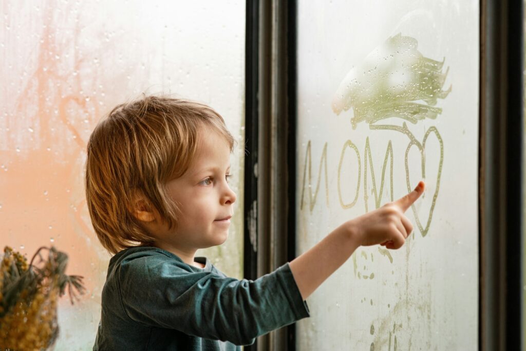 Cute kid drawing words on a dew covered window